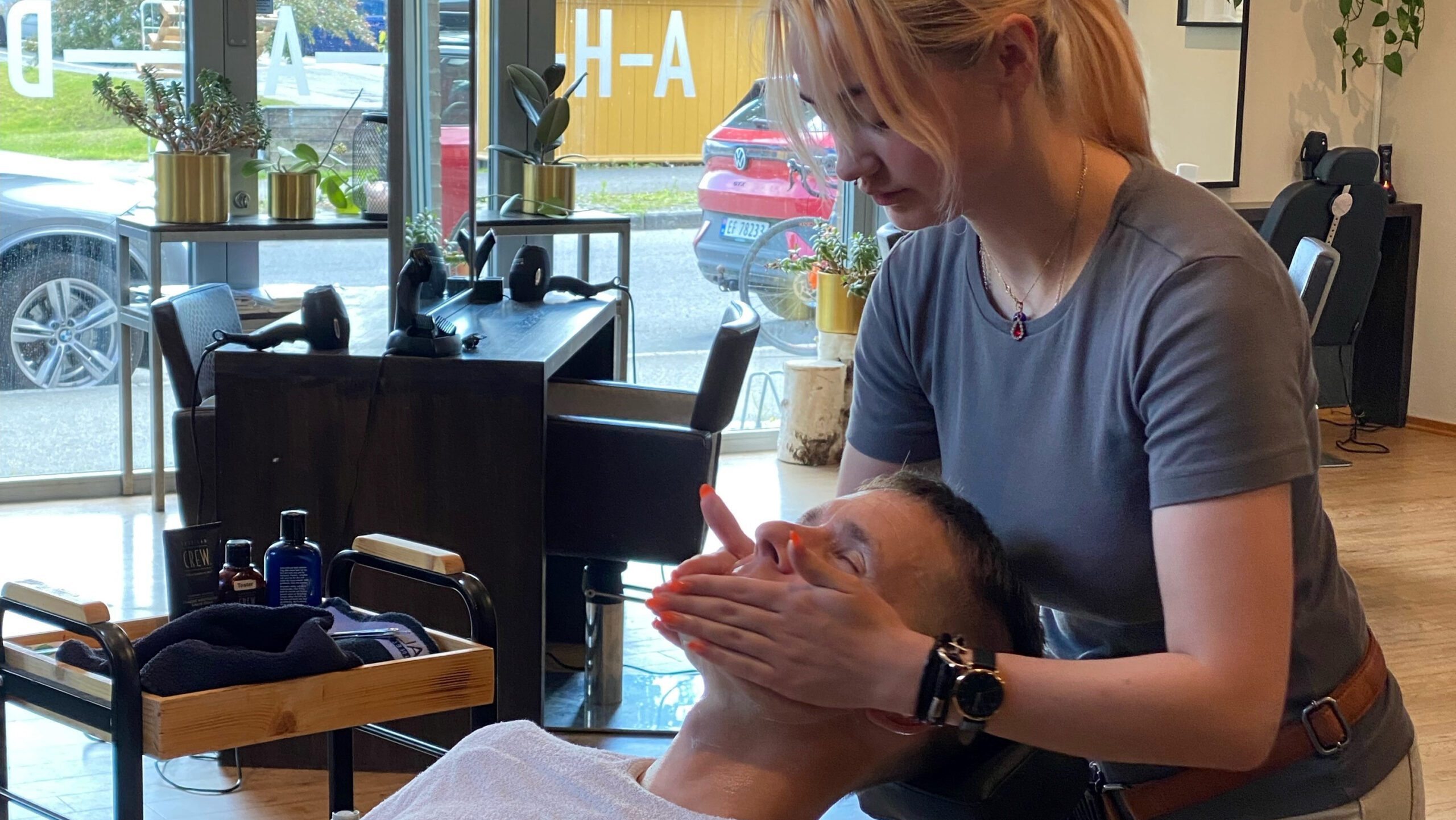 Bildet viser en frisør som gjør hår- og skjeggpleie på en mannlig kunde